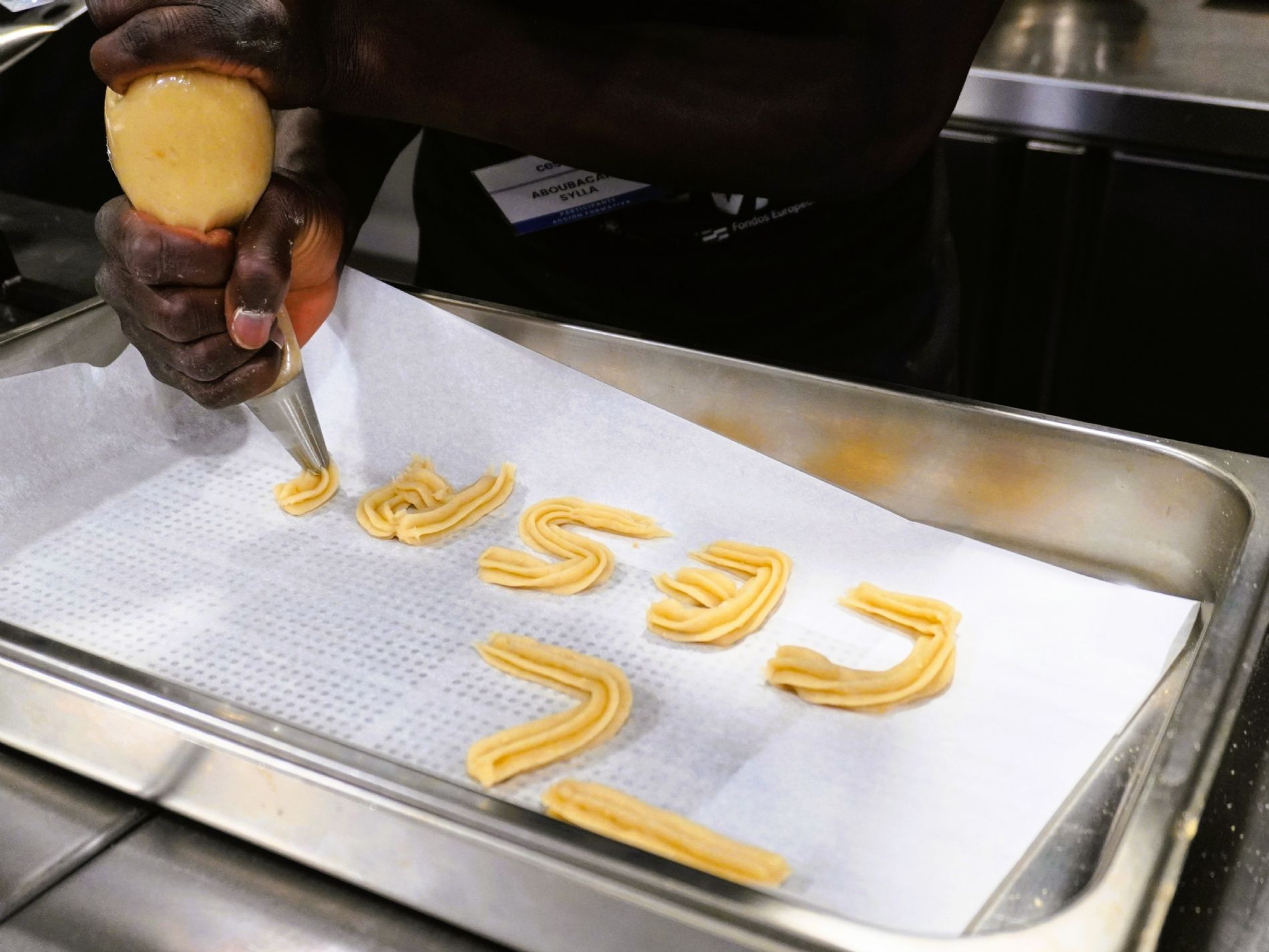 Con ayuda de la manga pastelera, un participante de la formaci�n de Ayudante de Cocina de Cesal da forma a las letras durante la elaboraci�n de los churros de gofio. / Foto: Cesal