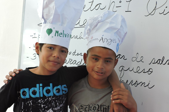 Dos nios con sombreros de cocinero abrazados a los hombros