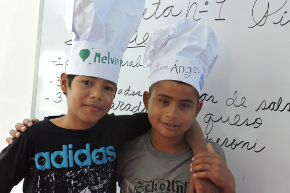 Dos niños con sombreros de cocinero abrazados a los hombros